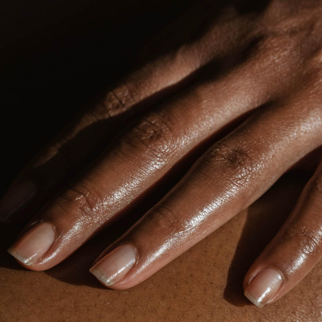 Nahaufnahme einer Hand mit natürlichen, sauberen Fingernägeln, die sanft auf einer Oberfläche ruht. Die Haut wirkt warm, glatt und gut befeuchtet, und subtile Licht- und Schatteneffekte verleihen dem Bild Tiefe.